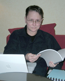 Reese in her hotel room with a computer on her lap, a notebook in her hands and another notebook near: She is working. Putting together a class, by the looks of it.